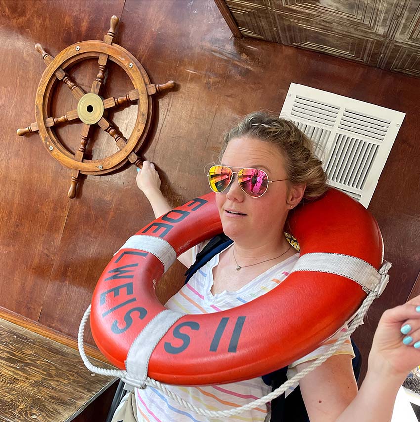 Lynne poses at the Edelweiss Cruises photoshoot with an old-fashioned ship steering wheel and a PFD.