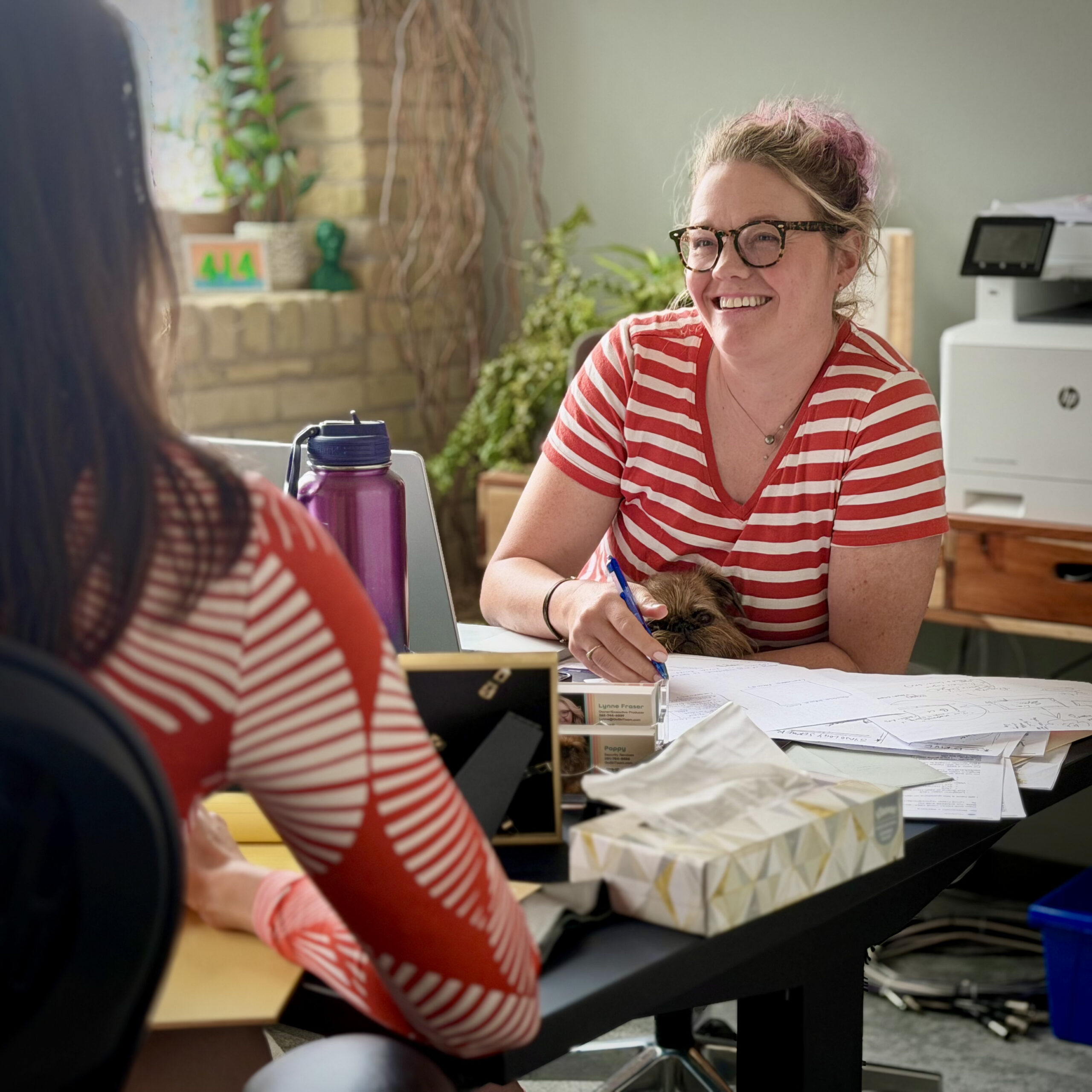 Lynne in her office consulting with a colleague, holding her dog, Poppy, in her lap